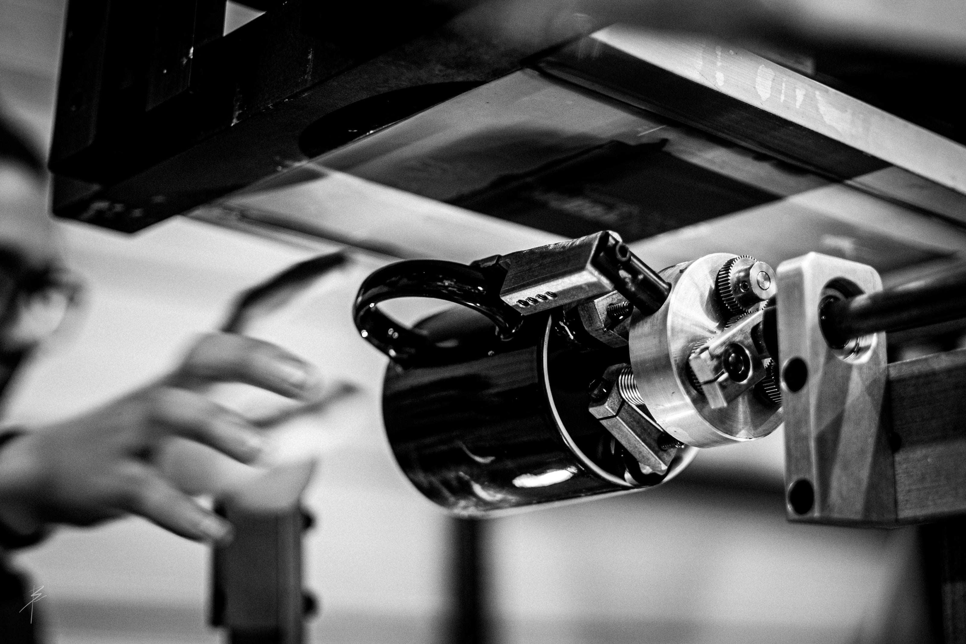 Close up of screen printing machine in action. A hand is about to grab a mug that is set in the screen printer.